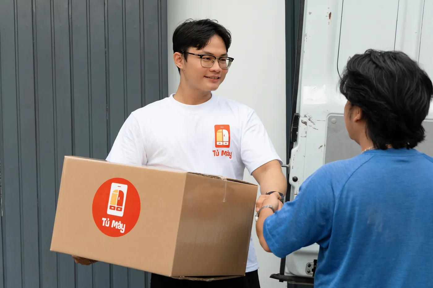 A Tủ Mây crew member handing a branded box to a customer beside the van