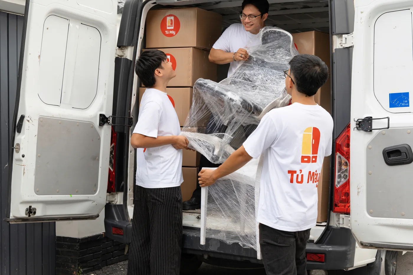Two crew members lifting a shrink-wrapped chair into the van