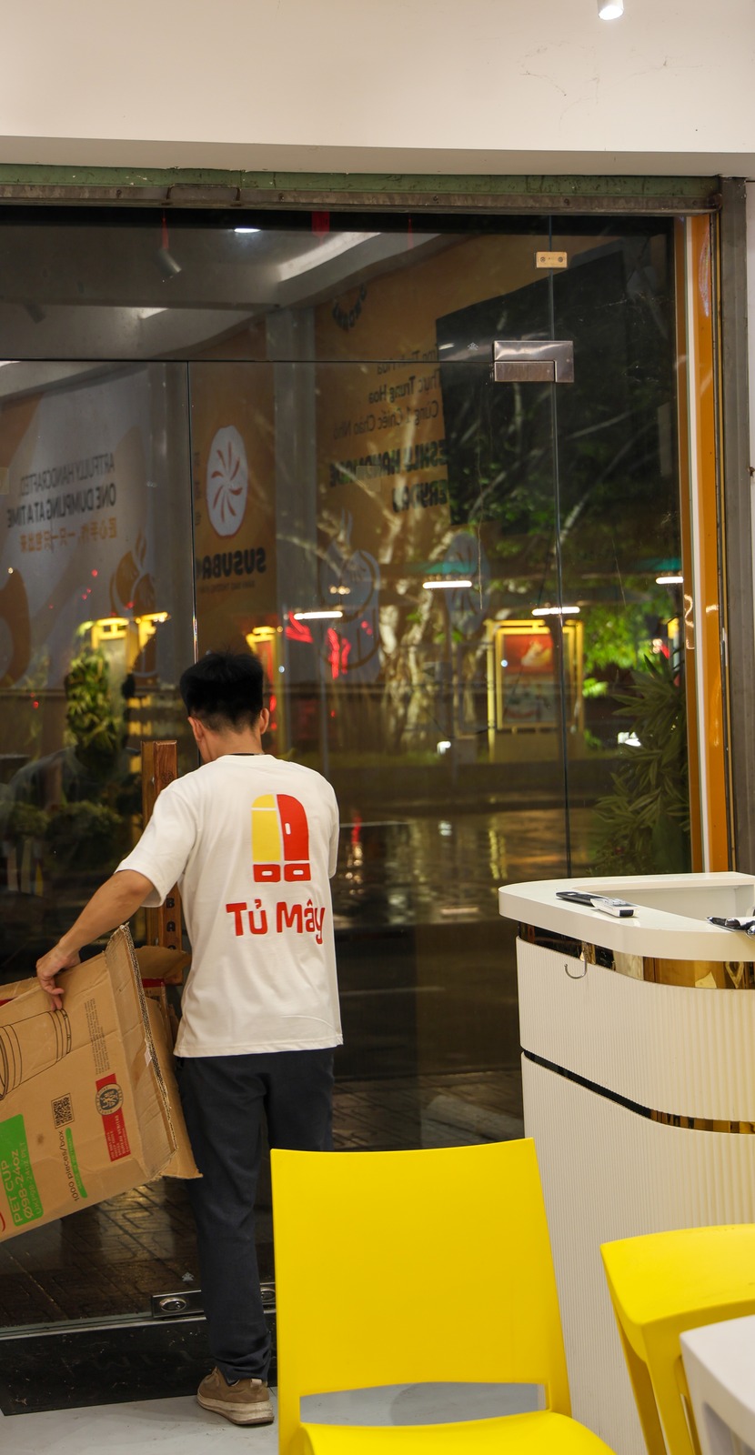 A crew member carrying a box out through the glass front at night