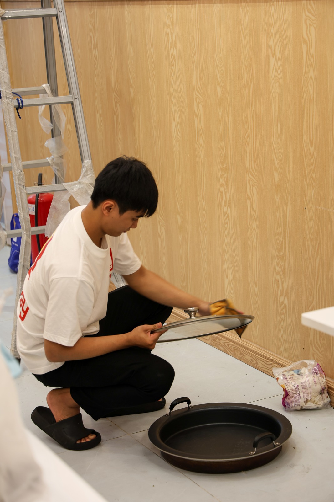 A crew member crouching to clean a pan and its glass lid