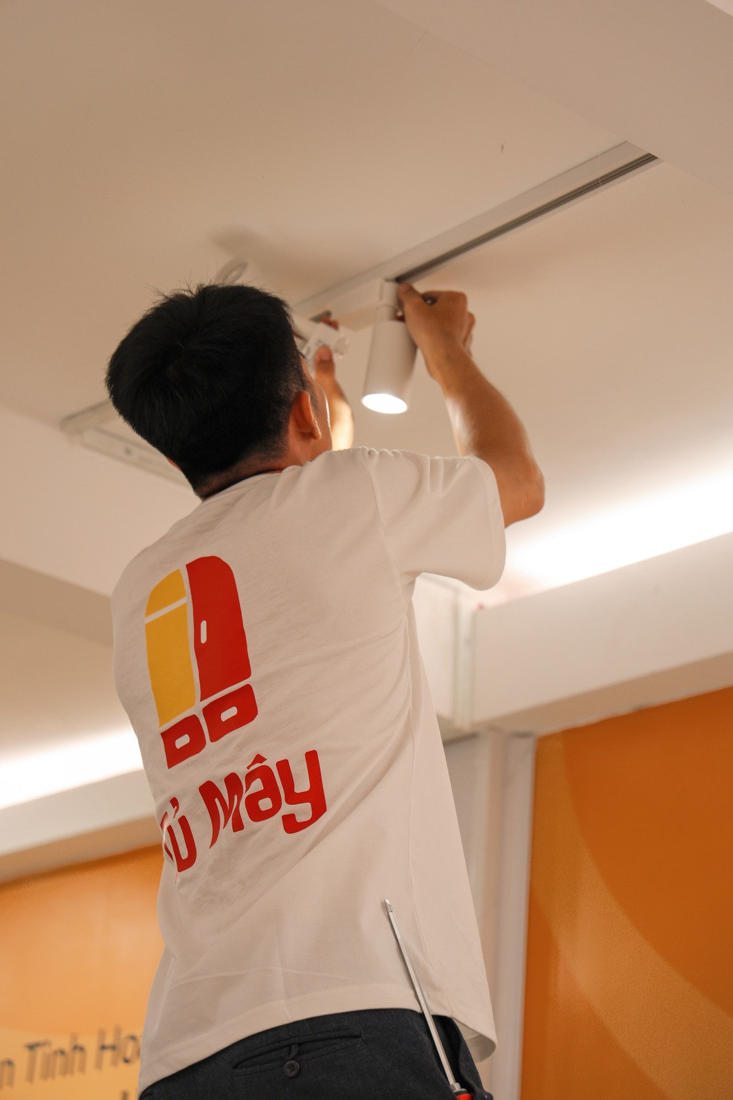 A crew member removing a track light head from the ceiling