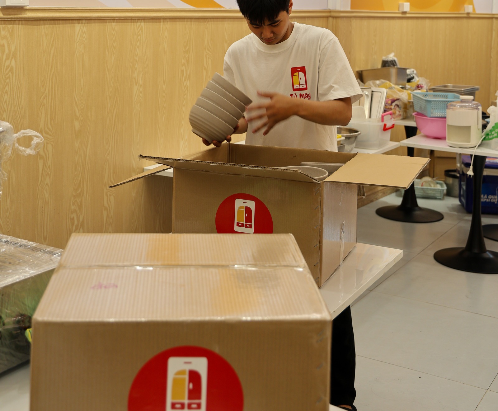 A crew member stacking bowls into a box, a sealed box in the foreground
